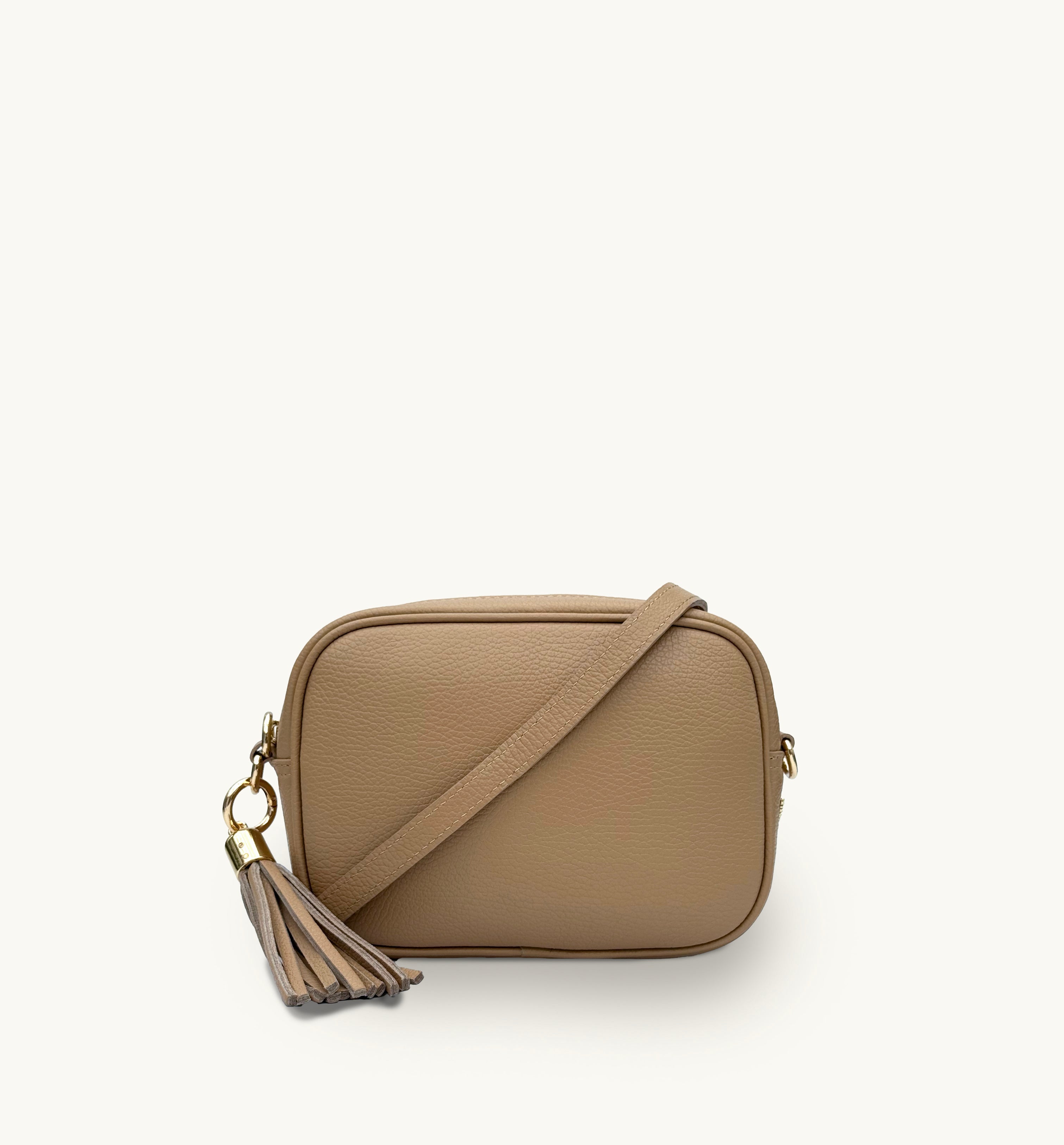 A sand leather crossbody bag with a tassel detail on the strap, displayed against a plain background.