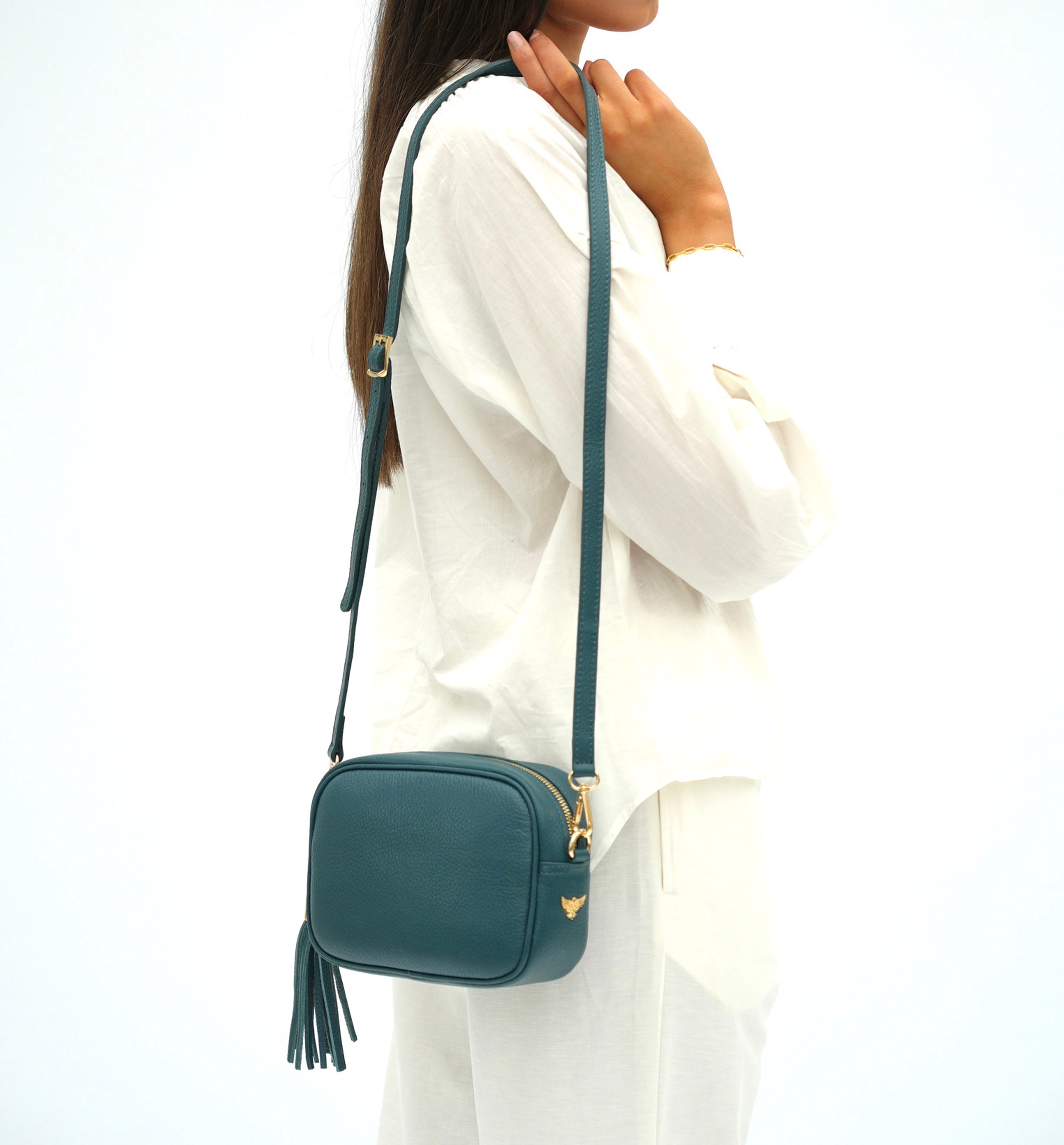 Person wearing a teal crossbody bag with a visible brand logo on a white background